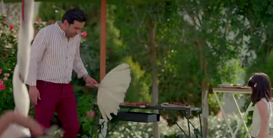 Man and woman standing outdoors with a grill and table in a garden setting votagrills charcoal grill m شوايه فحم فوتا للحدبقه معدن 